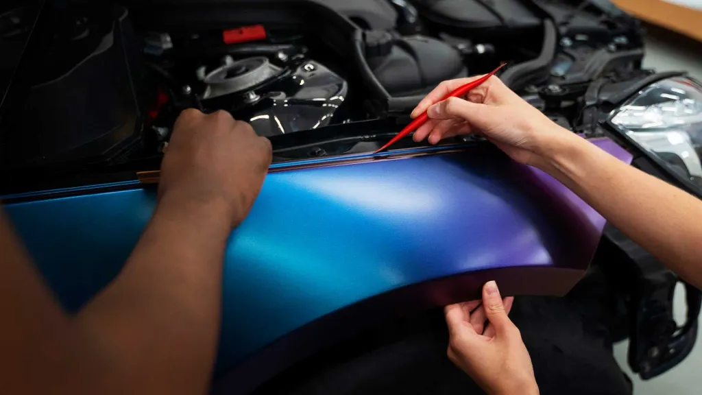 Installers carefully applying a color-shift vinyl car wrap to a vehicle panel using professional tools.