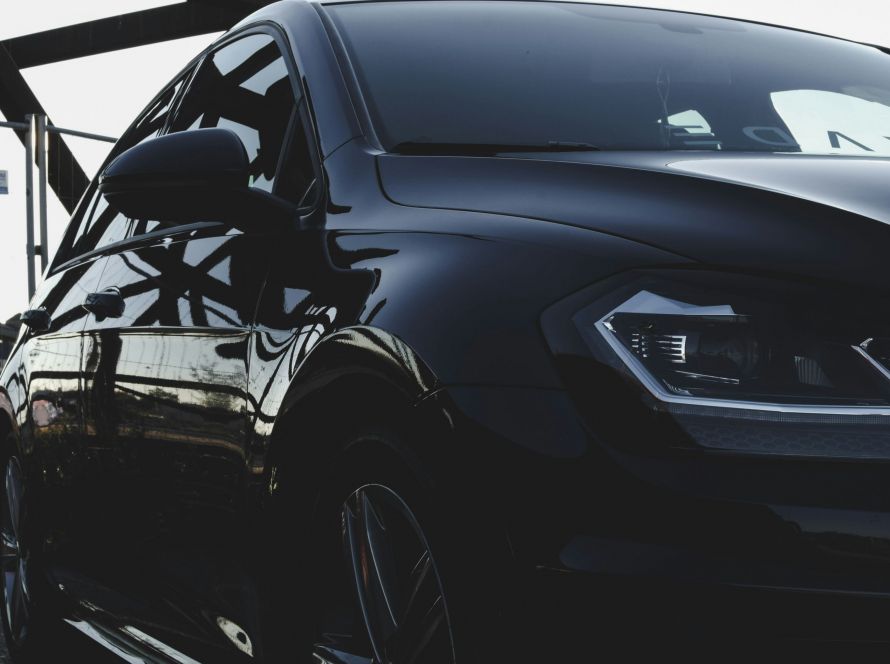 A close-up side profile of a dark car parked outdoors, showcasing the appearance of window glass treated with ceramic tint.