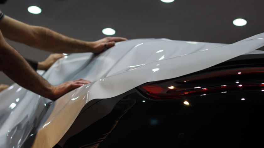 Two technicians carefully applying a white vinyl car wrap onto the hood and side of a modern vehicle in a workshop.