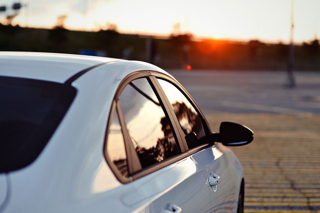 A white sedan parked outdoors at sunrise, highlighting the clear appearance of ceramic tint on the side windows.